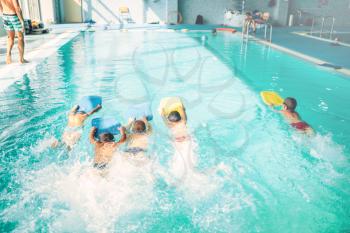 Boys swimming with plank in a pool race. Children in water with plank are doing swim exercise. Healthy sport activity in pool. Sportive kids activity in modern sport center with pool.