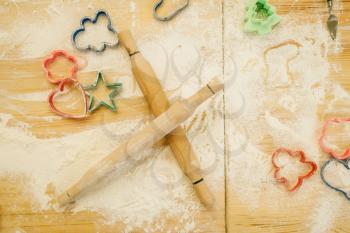 Cookie cutters, rolling pin and flour on wooden table, top view, nobody. Hearts, stars and gingerbread man, pastry templates on the countertop, bakery forms