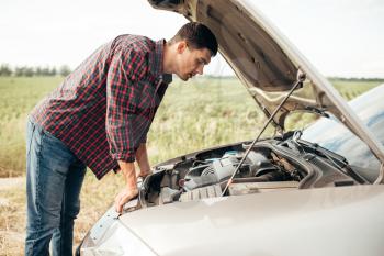 Tired man tries to repair a broken car. Vehicle with open hood on roadside