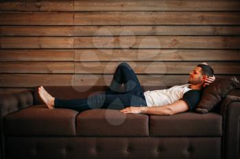 Young happy man lying on couch, side view. Relaxation on sofa. Male person relax