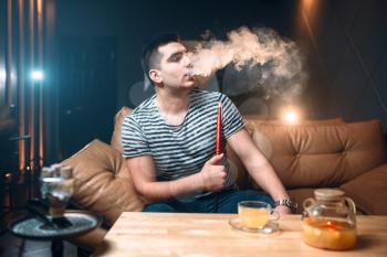 Young man smoking and relaxation at hookah bar. Tobacco smoke, night lifestyle