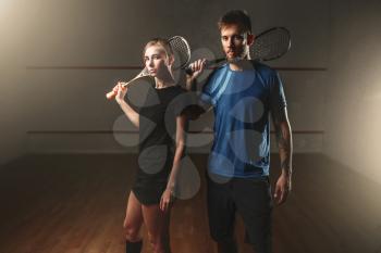 Male and female squash game players with rackets. Young couple in sportswear with racquets, indoor sport club