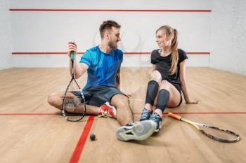 Squash game concept, rackets with ball, young couple sitting on the floor after active training, indoor sport club