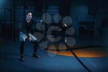 Sportsman on training, workout with battle ropes in gym. Energy exercises in sport club