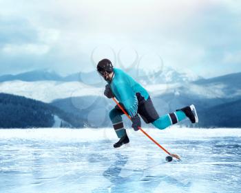 Professional ice hockey player in uniform exercise on frozen lake, winter forest on background. Ice-skating outdoors