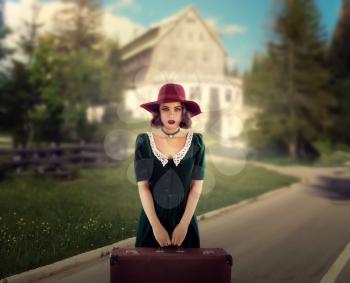 Female traveler in retro red hat and green dress holds suitcase in hands. Young woman travels, vintage style fashion. Summer journey 