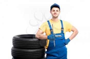Serviceman in blue uniform sitting on tires, white background, repairman with tyres