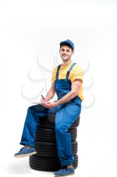 Tyre service worker sitting on a pile of tires, white background, repairman, wheel mounting