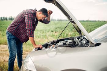 Tired man tries to repair a broken car. Vehicle with open hood on roadside