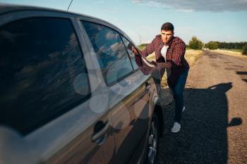 Man pushing broken car. Vehicle with trounble on roadside in summer day