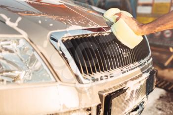 Male hand rubbing the car with foam, automobile in suds. Carwash station