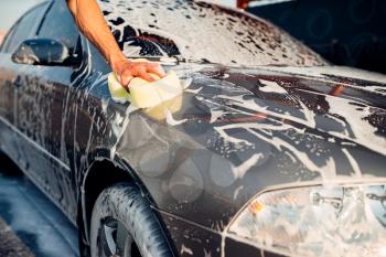 Male hand rubbing the car with foam, automobile in suds. Carwash station