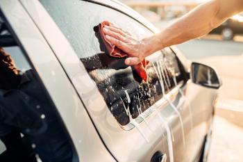 Male hand rubbing vehicle window with foam, automobile in suds, car wash. Carwash station