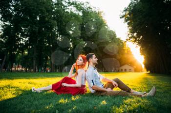 Love couple sits on a grass in summer park. Romantic date of attractive woman and young man