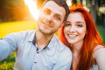 Selfie of love couple in summer park on sunset. Romantic date of attractive woman and young man