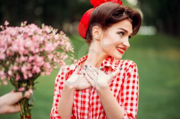 Glamour pinup girl takes gift a bouquet of flowers, retro american fashion. Attractive woman in pin up style