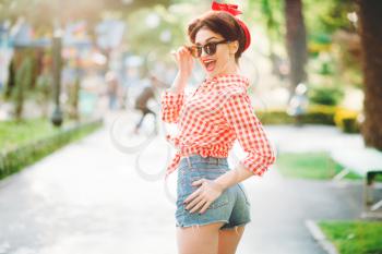 Sexy pinup girl in denim shorts and sunglasses outdoors, retro american fashion. Attractive woman in pin up style