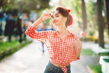 Sexy pin up girl with lollipop in hand walks in a park, retro american fashion. Attractive woman in pinup style