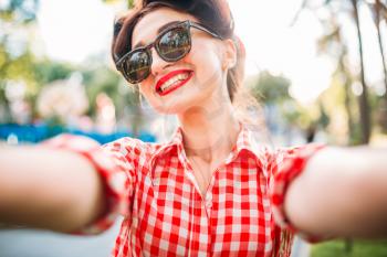 Pinup girl in sunglasses, selfie shot outdoors, fifties american fashion. Attractive model in pin up style