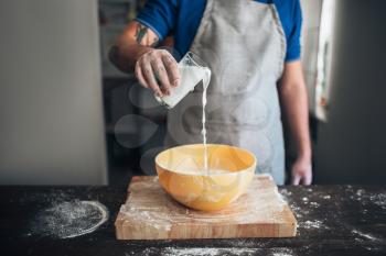 Male baker hands adds milk to the bowl. Bread preparation. Homemade bakery. Recipe ingredients