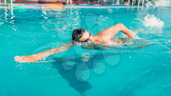 Athletic swimmer in glasses swims in indoor swimming pool. Aqua sports exercise