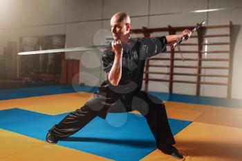 Wushu master training with sword, martial arts. Man in black  cloth poses with blade