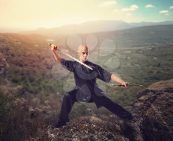 Wushu master with sword, meditation on the top of mountain, martial arts. Man in black  cloth poses with blade
