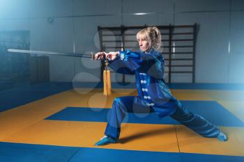 Female wushu fighter with sword in action, martial arts. Woman in blue cloth poses with blade