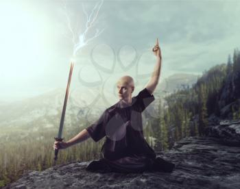 Wushu master with blade, lightning control on the top of mountain, martial arts. Man in black  cloth poses with sword