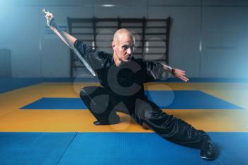 Wushu master training with sword, martial arts. Man in black cloth poses with blade