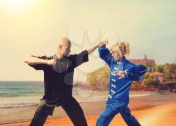 Male and female wushu fighters training on sea coast, martial arts. Sparring partners in action outdoor