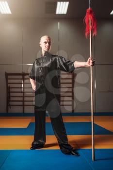 Wushu fighter poses with lance, martial arts. Man in black  cloth poses with blade
