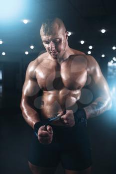 Muscular male athlete posing with dumbbell in sport gym. Fitness training with weight. Bodybuilding workout