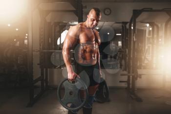Strong male bodybuilder with pancakes from barbell. Exercise with barbell in sport gym. Fitness training with weight. Bodybuilding workout