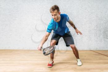 Squash game training, male player with racket and ball, indoor court on background