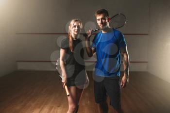Male and female squash game players with rackets. Young couple in sportswear with racquets, indoor sport club