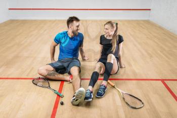 Squash game concept, rackets with ball, young couple sitting on the floor after active training, indoor sport club