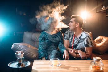 Man with hookah blows smoke in the womans face. Love couple leisure, relaxation and smoking shisha