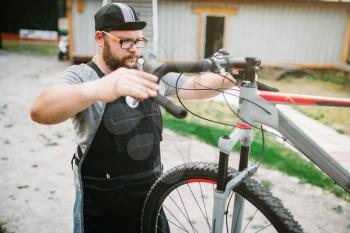 Mechanic adjusts the bicycle handlebars and brakes. Cycle workshop outdoor. Bicycling sport, bearded service man work with wheel