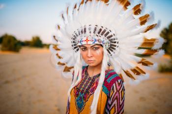 Young American Indian woman in traditional costume and headdress made of feathers of wild birds
