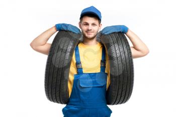 Tire service worker in blue uniform holds car tyres in hands, white background, repairman, wheel mounting