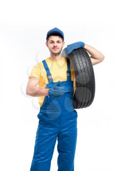 Service worker in blue uniform holds car tire in hand, white background, repairman with tyre, wheel mounting