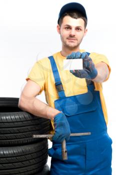 Tyre service, worker in blue uniform holds tire and empty businesscard in hands, white background, repairman, wheel mounting