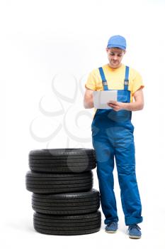 Tyre service worker in uniform with notebook against pile of tires, white background, repairman, wheel mounting