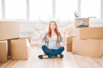 Smiling woman sitting on the floor among cardboard boxes, housewarming. Relocation to new home