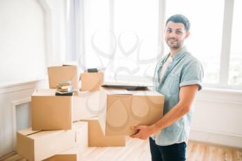Smiling young man holds carton box in hands, housewarming. Moving to new house