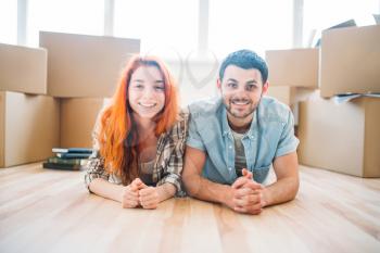 Smiling couple lies on the floor among cardboard boxes, moving to new house, housewarming
