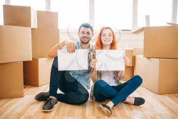 Happy couple sitting on the floor with empty paper sheets in hands, moving to new home, housewarming