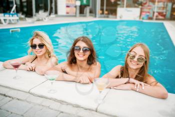 Three happy girls in swimsuits and sunglasses on the poolside. Resort holidays. Attractive women in the swimmimg pool