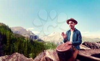 Young male drummer with wooden bongo drums plays on top of mountain, musician in motion. Djembe, musical percussion instrument, ethnic music
